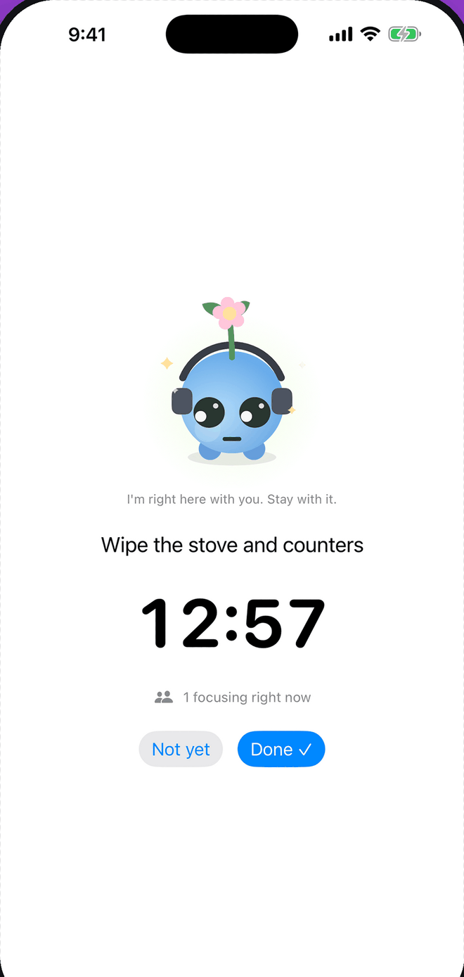 The Focable focus timer showing 12:57 left on the step "Wipe the stove and counters", with the companion sitting above it wearing headphones